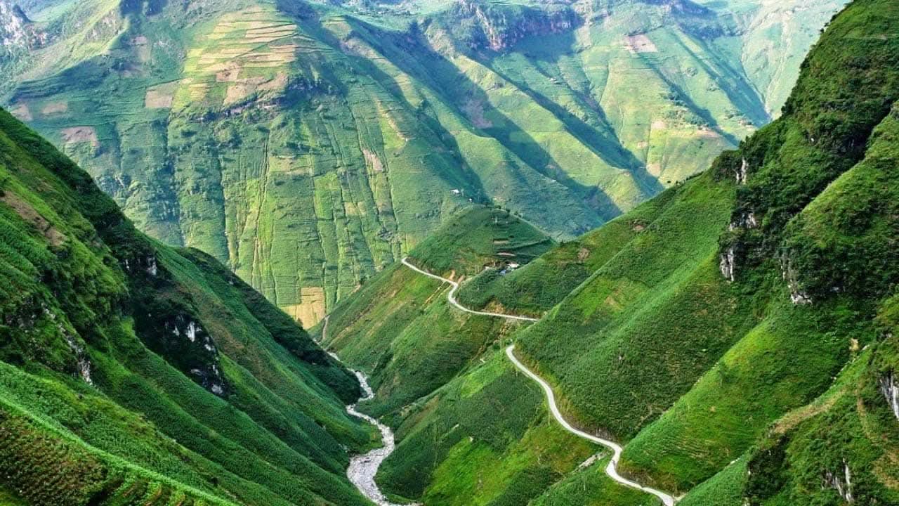A winding road and stream between green mountain slopes in Ha Giang